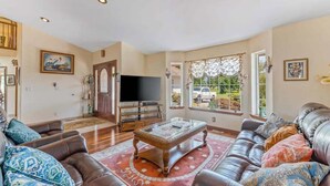 A living room with a leather sofa, a coffee table, and a television. - Spanish-style 6BR Mountainview - Deck - W&D (East Wenatchee)