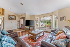 A living room with a leather sofa, a coffee table, and a television. - Spanish-style 6BR Mountainview - Deck - W&D (East Wenatchee)