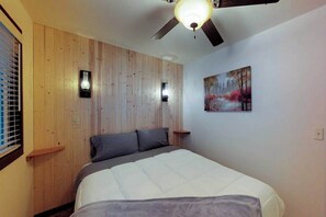 Une chambre à coucher avec un lit, un mur recouvert de panneaux en bois, un ventilateur de plafond et un tableau.