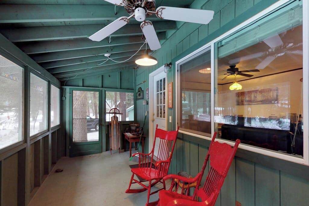 Une pièce avec un ventilateur de plafond, une fenêtre donnant sur un beau paysage et un fauteuil rouge.