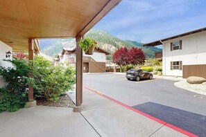 A building with a covered entrance, a parking area, and a mountain backdrop. - Downtown Studio 1st-Floor - Icicle Village Resort (Leavenworth)