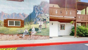 A building with a mural depicting a rural scene, a wooden balcony, and a red curb indicating a parking area. - Downtown Studio 1st-Floor - Icicle Village Resort (Leavenworth)