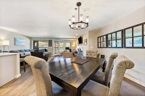 Een ruime eethoek met een donkerhouten tafel en comfortabele stoelen, een kroonluchter erboven en uitzicht door grote ramen.