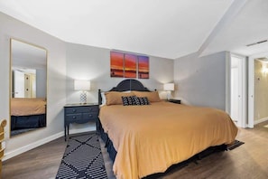A bedroom with a bed, bedside tables, a mirror, and a painting on the wall.