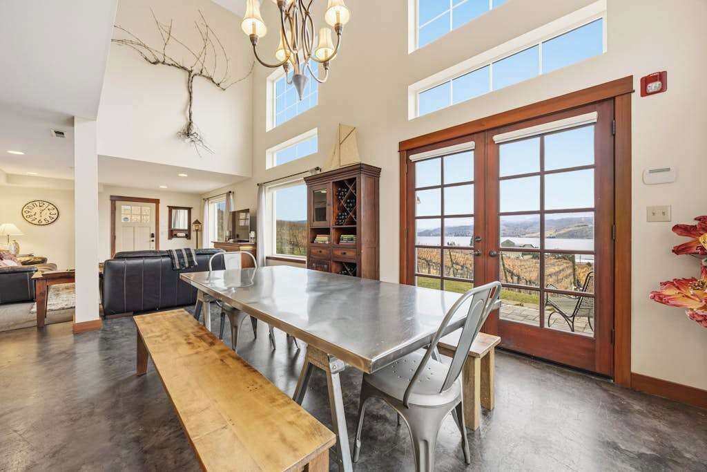 A spacious dining area with a long table, chairs, and a bench. There is a large window with a view of the outdoors.