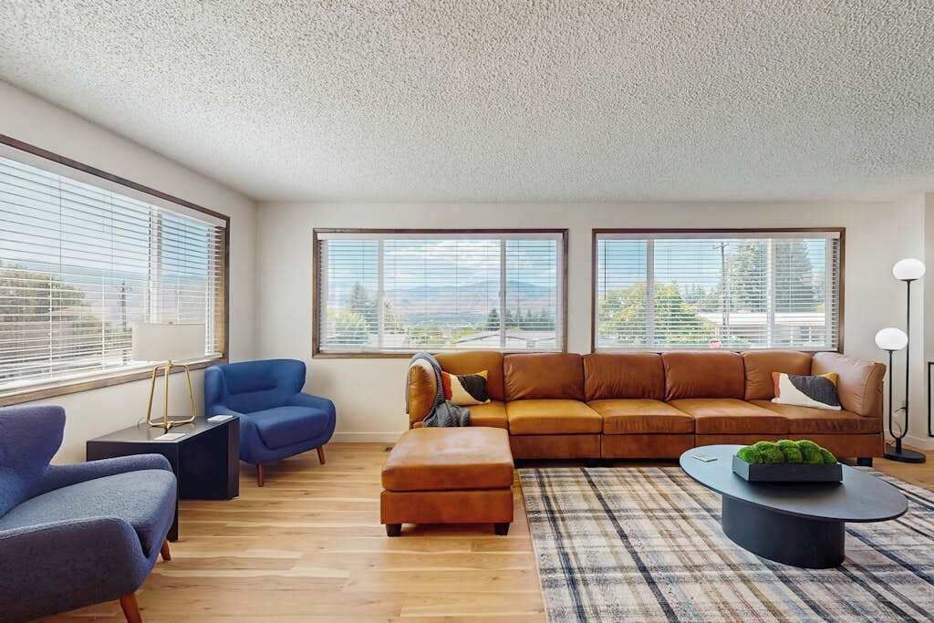 A modern living room with a sectional sofa, two armchairs, a coffee table, and a view through large windows.