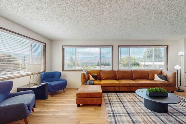 Una sala de estar moderna con un sofá modular, dos sillones, una mesa de centro y vistas amplias a través de grandes ventanales.
