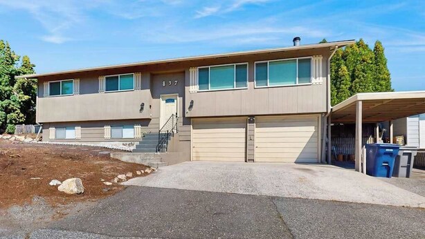 A two-story building with a garage, a covered parking area, and a dirt driveway. - 3BR Home & Bunk Room with hot tub, mountain views (East Wenatchee)