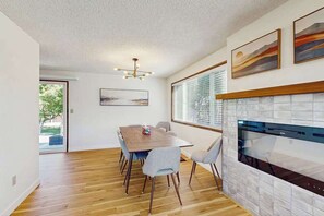 A dining area with a wooden table and chairs, a fireplace, and artwork on the wall. - 3BR Home & Bunk Room with hot tub, mountain views (East Wenatchee)