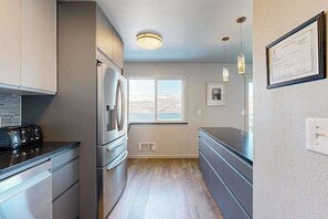 A modern kitchen with stainless steel appliances, a window with a view, pendant lighting, and a framed certificate on the wall. - Updated 3BR Lakeview - Balcony - Washer/Dryer (Chelan)