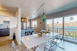 A modern kitchen with a white countertop, stainless steel appliances, and a dining area with a white table and clear chairs.