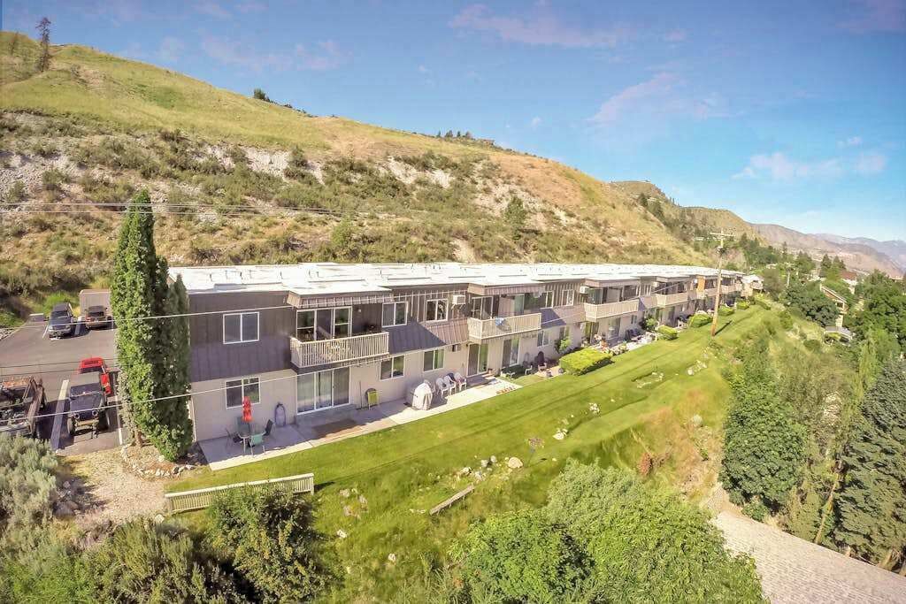 Un immeuble à plusieurs étages, doté d’un toit plat, entouré d’une pelouse bien entretenue et d’un paysage vallonné.