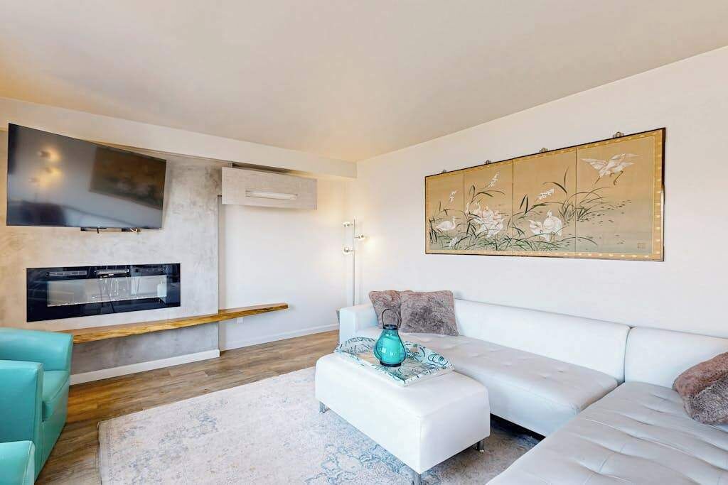 Un salon moderne avec un canapé blanc, un fauteuil d’accent de couleur turquoise, un téléviseur à écran plat et un tableau décoratif.