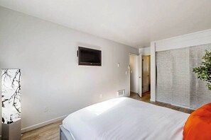 A bedroom with a bed, a television mounted on the wall, and a sliding door leading to another room.