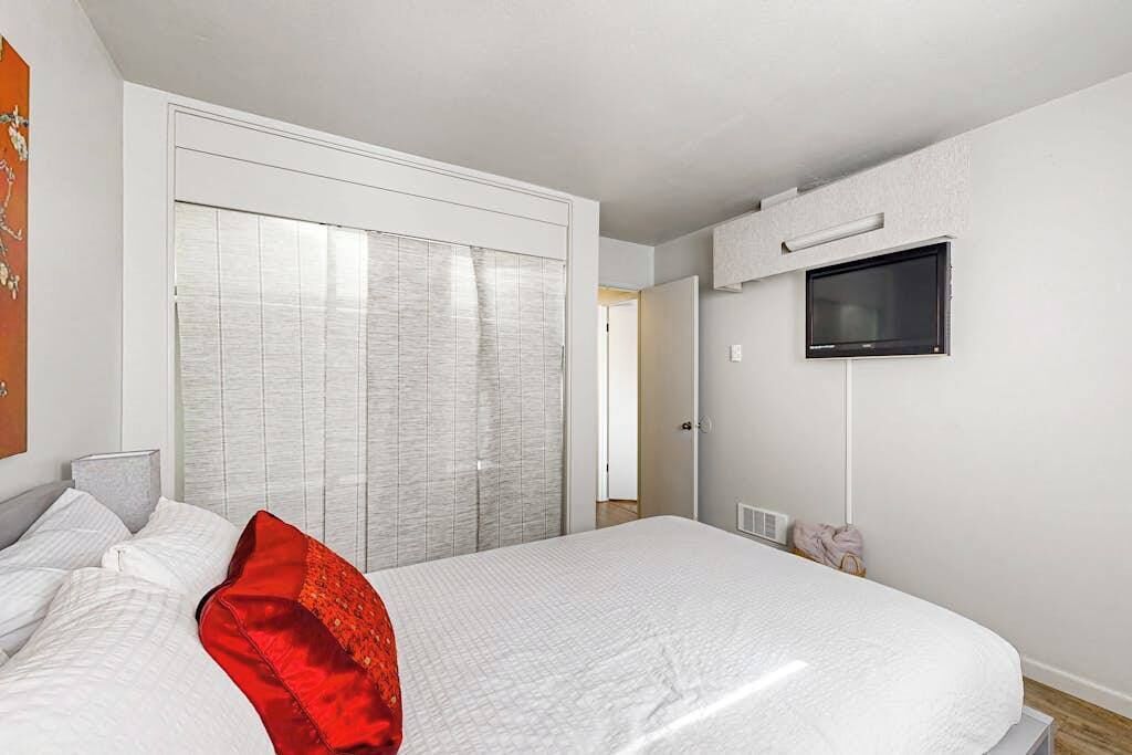 Une chambre d’hôtel avec un lit, un téléviseur fixé au mur et une porte coulissante donnant sur une autre pièce.