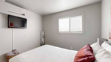 A bedroom with a bed, a television mounted on the wall, a window, and a wall-mounted air conditioning unit.
