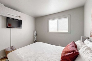 A bedroom with a bed, a television mounted on the wall, a window, and a wall-mounted air conditioning unit.
