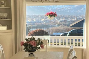 A dining area with a table and chairs, a hanging flower arrangement, and a view of a cityscape with mountains in the background. - 4BR family friendly house with pool, hot tub, W&D (East Wenatchee)