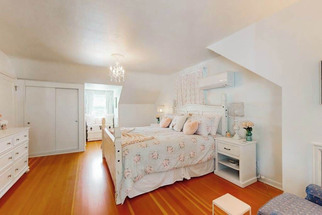 Une chambre à coucher avec un lit, des tables de chevet, une commode, un lustre et une fenêtre.