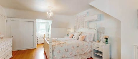 Une chambre à coucher avec un lit, des tables de chevet, une commode, un lustre et une fenêtre.