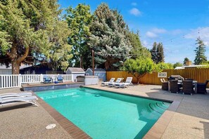 A rectangular swimming pool with a tiled edge, surrounded by a wooden deck. There are lounge chairs and a barbecue area with a wooden fence in the background. - 4BR family friendly house with pool, hot tub, W&D (East Wenatchee)