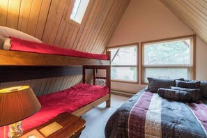 Une chambre de dortoir avec des lits superposés, une table de chevet avec une lampe et une fenêtre avec des stores.