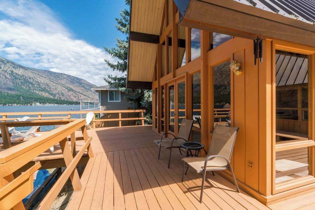 A wooden deck with outdoor seating, overlooking a body of water and mountains.