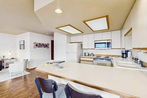A modern kitchen with white cabinetry, a central island, and a microwave above the stove. - 2BR lakeside condo with shared pools and hot tub (Chelan)