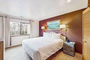 A hotel room with a large bed, a nightstand, a lamp, and a window with curtains. - 2BR lakeside condo with shared pools and hot tub (Chelan)