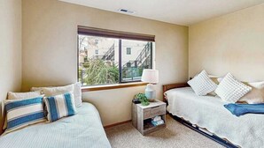 A hotel room with two beds, a window with a view of buildings, a small bedside table with a lamp, and a nightstand with a plant. - 2BR lakeside condo with shared pools and hot tub (Chelan)