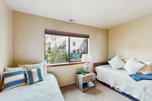 A hotel room with two beds, a window with a view of buildings, a small bedside table with a lamp, and a nightstand with a plant. - 2BR lakeside condo with shared pools and hot tub (Chelan)