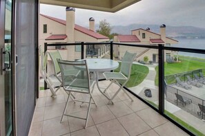 A balcony with a glass table and chairs, overlooking a lake and buildings. - Lovely 2BR Lakefront - Balcony - Pool (Chelan)