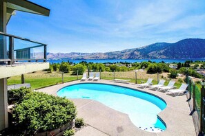 Une piscine avec des chaises longues, une vue sur les montagnes et un ciel dégagé.