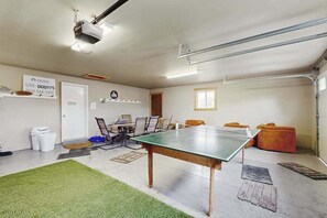 Ein Raum mit Tischtennisplatte, Projektor und einer Sitzecke mit Stühlen und Kissen.