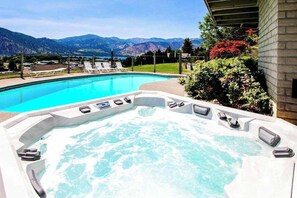 A hot tub with a pool and lounge chairs, surrounded by mountains and greenery.