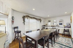 Un coin repas avec une table et des chaises en bois, une cuisine en arrière-plan et une fenêtre donnant sur un paysage.