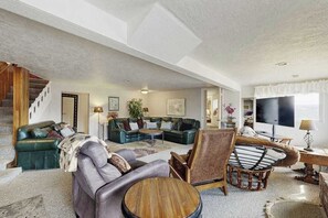 A spacious living room with a staircase, leather sofas, a wooden coffee table, and a large flat-screen TV.