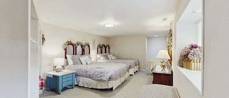 A bedroom with two beds, a bedside table, a nightstand, a mirror, and a wall-mounted shelf with flowers.