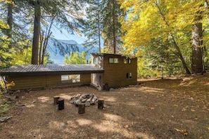 A cabin with a small deck and a fire pit in a forested area. - Lake-view 3BR - private hot tub, dog-friendly (Leavenworth)