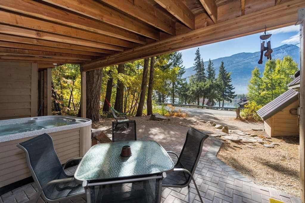 A wooden deck with a hot tub, outdoor seating, and a view of trees and mountains.