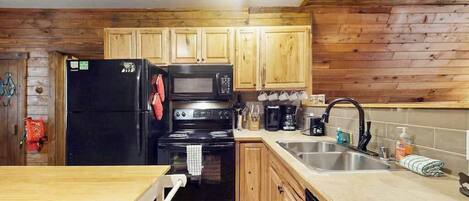 A kitchen with wooden cabinets, a black refrigerator, a microwave, a stove, and a sink.