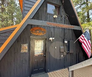 A cabin with a dark wooden exterior, a front door, and an American flag. - Studio Cabin - hot tub, near skiing, dogs welcome (Leavenworth)