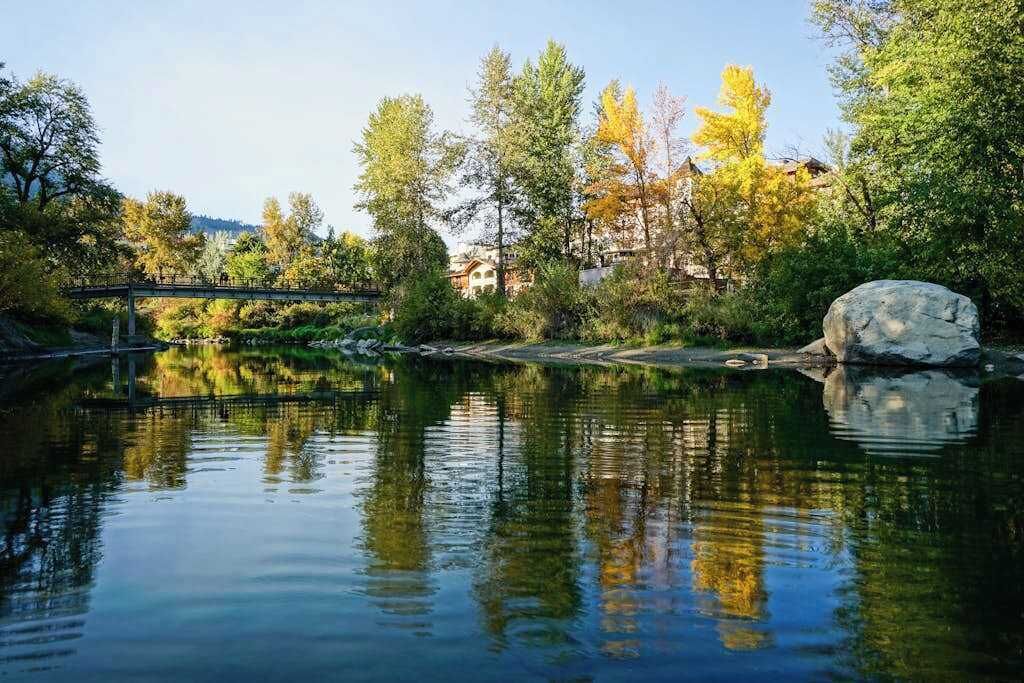A tranquil riverside setting with a bridge, trees, and a large rock.