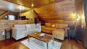 Ein gemütliches Blockhauss-Interieur mit Holzbalkendecke, einer Couch, einem Couchtisch und einer Küchenzeile.