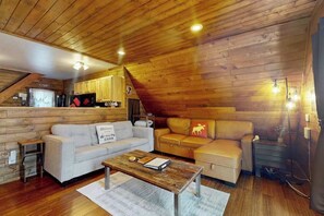A cozy cabin interior with a wooden ceiling, a sofa, a coffee table, and a kitchenette. - Studio Cabin - hot tub, near skiing, dogs welcome (Leavenworth)