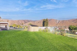 A residential area with a well-maintained lawn, a small shed, and houses in the background with a mountainous landscape.