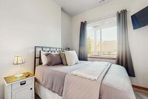 A bedroom with a bed, bedside table, lamp, and a window with curtains. - Three BR home with great views & location (Orondo)
