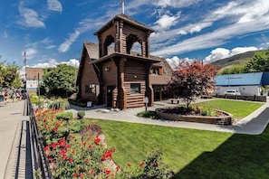 A wooden log cabin with a bell tower, surrounded by a well-maintained garden with red flowers. - Charming 2BR Lakefront - Patio - Pool (Chelan)