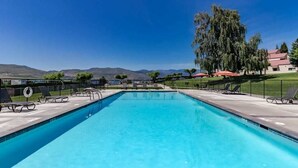 A rectangular swimming pool with a clear blue water surface, surrounded by a concrete deck with lounge chairs and umbrellas. - Charming 2BR Lakefront - Patio - Pool (Chelan)