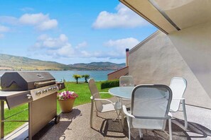Eine Terrasse im Freien mit Grill, Stühlen und Blick auf einen See und Hügel.